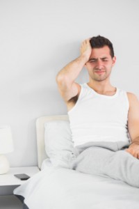 Man with headache sitting in bed: CannaLinq CBD Oil Blog